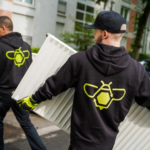 Two men in black hoodies carrying radiators on a residential street