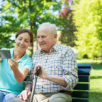 Woman showing smartphone to elderly man while sitting on a park bench.