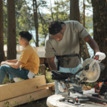 Two men working in a forest setting with construction tools and wooden beams.