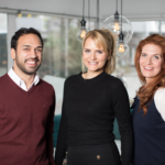 The three startup founders of Volunteer Vision smiling and posing indoors in a modern office setting.