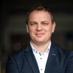 Founder of Fenecon in a suit with arms crossed, smiling confidently.