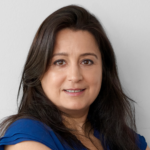 Woman with long dark hair in a blue blouse looking confidently