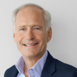 Older man with white hair in shirt and jacket smiling