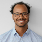 Man with glasses, short curls, and light blue shirt smiling