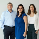 Three people posing in front of a light-colored wall, smiling at the camera.