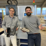 Two men in a battery lab holding e-bike battery components.