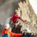 Two climbers with helmets and gear on a snowy mountain ridge