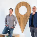 The two Followfood founders, formerly known as Followfish, standing next to a wooden location icon on a wall