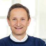 Portrait of Helmut Hildebrandt from OptiMedis in a navy sweater, smiling