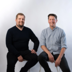 Portrait of two Gardia founders, previously known as carea, Micheal Hummels and Marlon Besuch sitting in front of a white wall, smiling confidently