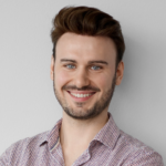 Young man with dark hair and beard smiling in a patterned shirt