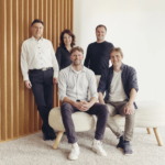 Five people standing and sitting in a modern office space with wood panel accents.