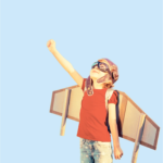 Child wearing cardboard wings and aviator goggles, pretending to fly