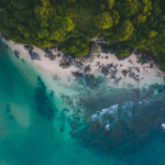 Aerial view of a tropical coastline with clear turquoise water and dense green forest