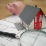 Model house on top of architectural plans with magnifying glass and piggy bank.
