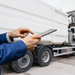 Person in blue uniform using a tablet in front of a white industrial truck.