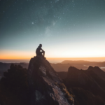 Silhouette of a person sitting on a mountain peak during sunrise